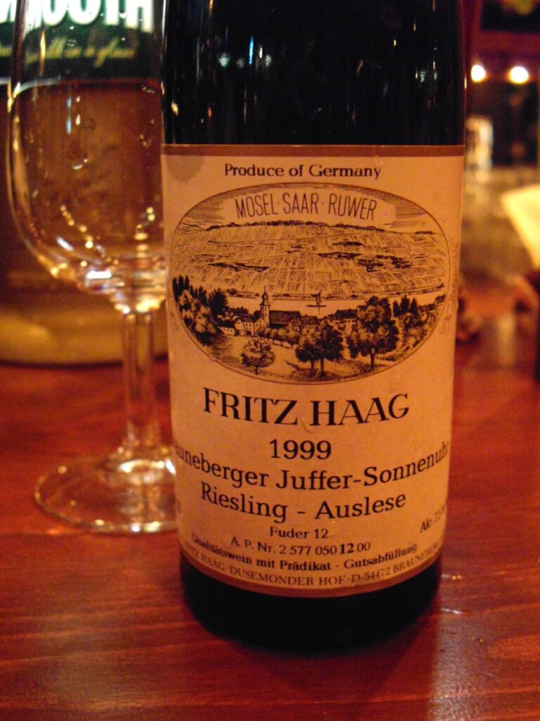 Bottle of Riesling Auslese next to a glass of wine on a table, emphasizing the wine's luxurious appearance and setting