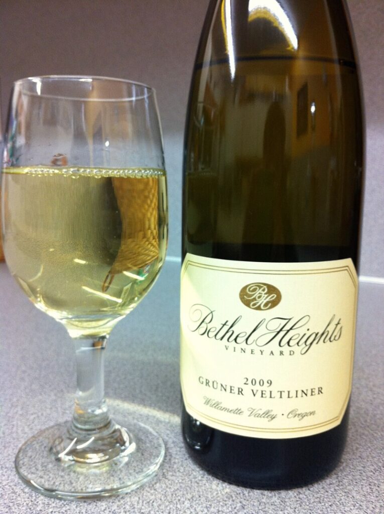 Bottle of Bethel Heights Gruner Veltliner beside a filled wine glass, showcasing a rustic wooden background.