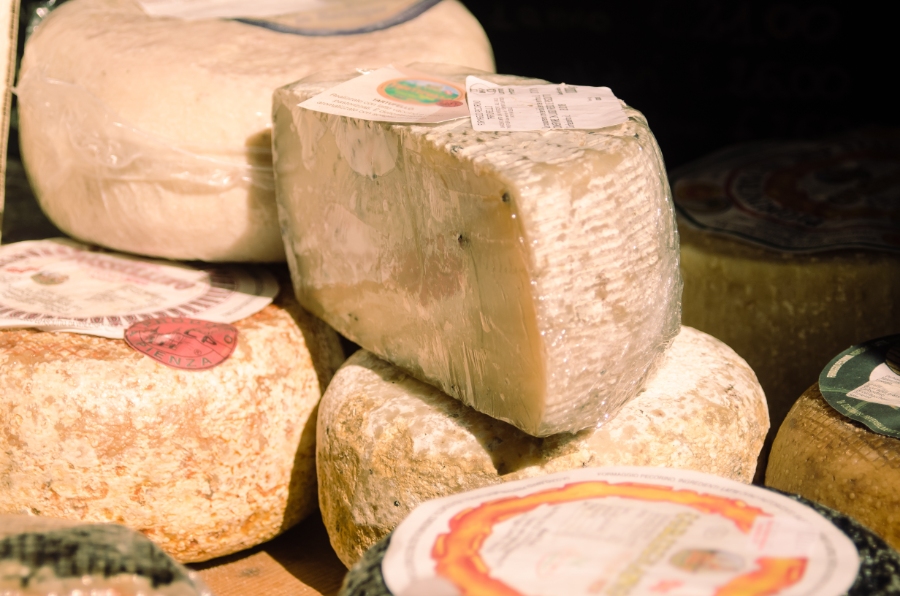 Close-up of a pile of Pecorino cheese displayed on a wooden shelf, showcasing its texture and color variations.
