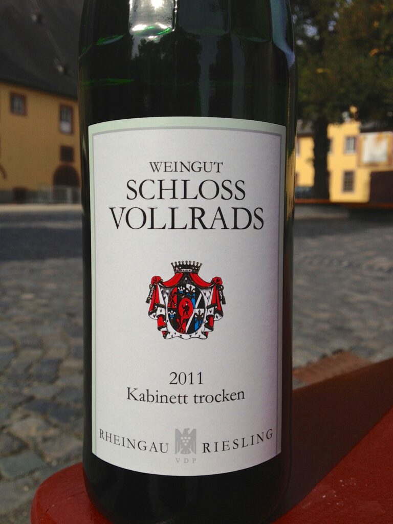 Bottle of Schloss Vollrads Riesling Kabinett Trocken placed on a wooden bench, showcasing its elegant label and design.