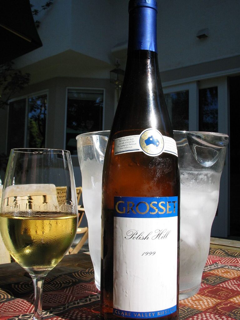 Bottle of Grosset Riesling and a filled glass of wine on a wooden table, showcasing the wine's color and clarity.