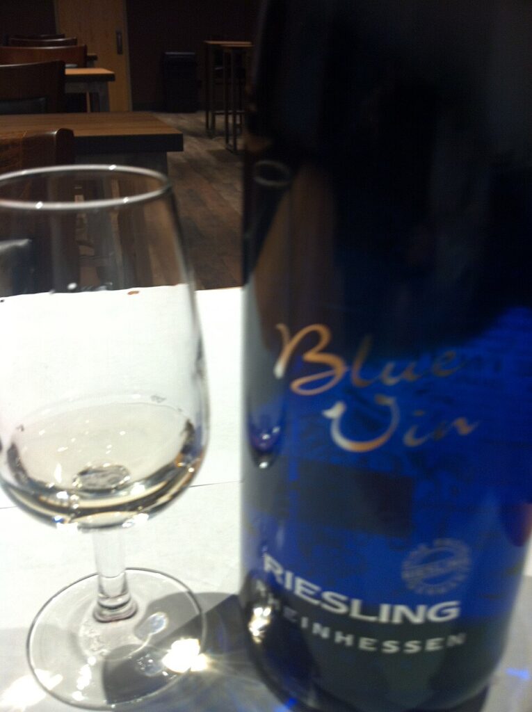 Bottle of Rheinhessen Riesling wine beside a filled glass on a wooden table, showcasing the wine's color and clarity.